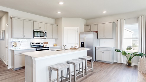 Kitchen with gray, shaker-style cabinetry, white quartz countertops, stainless-steel appliances, and an island with countertop seating.