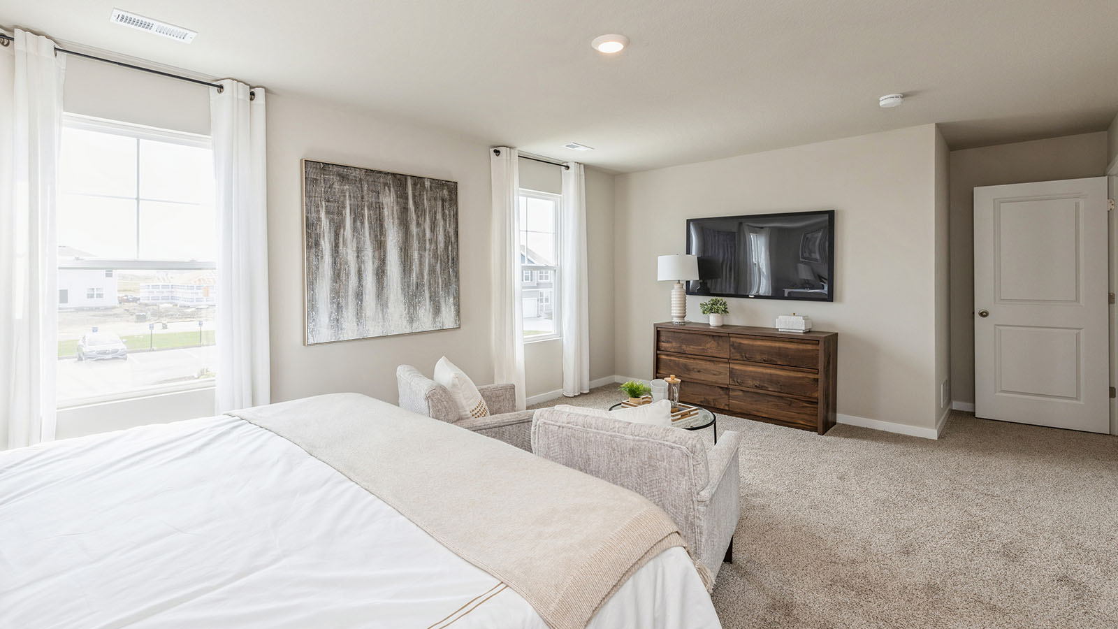 Bright primary bedroom with seating area and mounted tv
