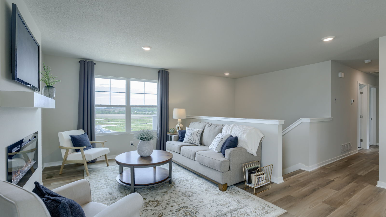 Spacious living room with brown flooring, white walls, a black fireplace and windows