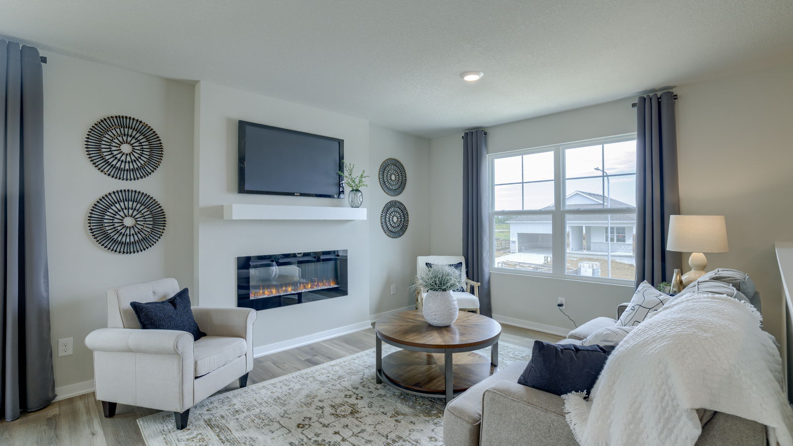 Spacious living room with brown flooring, white walls, a black fireplace and windows