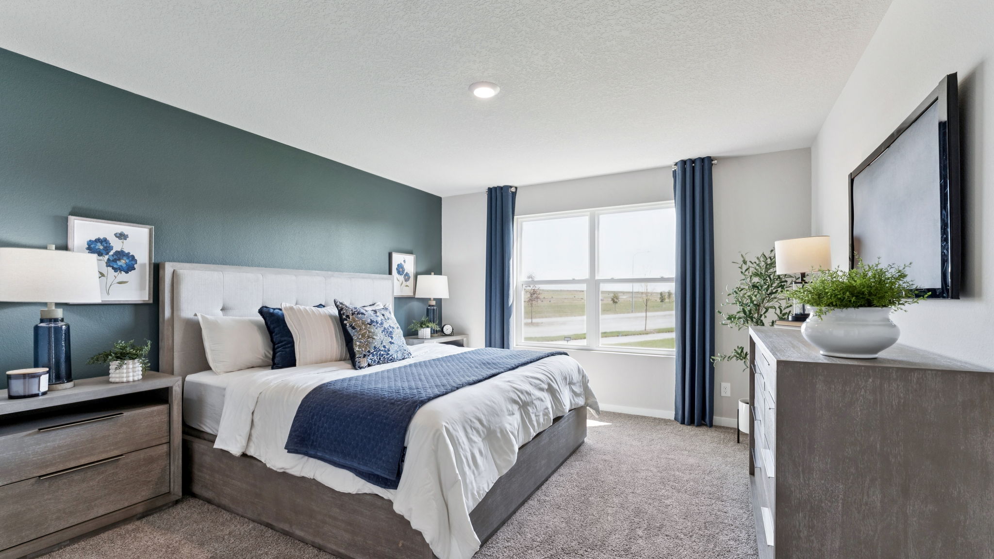Master bedroom of Hamilton with blue accent wall and large window for natural light.