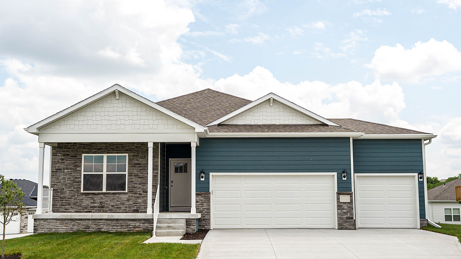 Exterior of the Neuville with blue siding, grey stone, and covered front porch with a three car garage