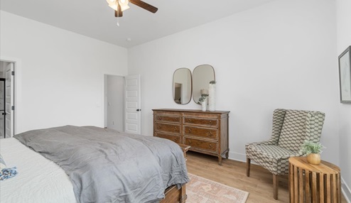 Master bedroom corner showcasing a wooden dresser with mirror above. To the side is a patterned chair with a side table.