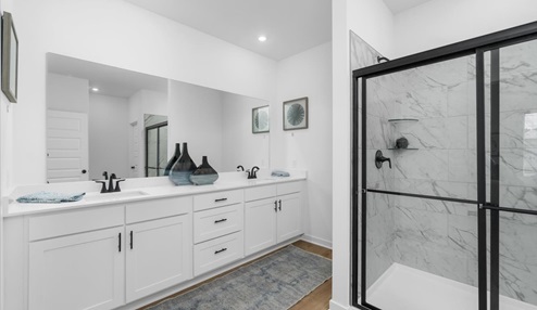 Master bathroom with double sinks on white cabinets with black ascents. Large walk-in shower with marble tile and black ascents.