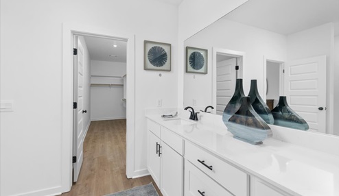 Master bathroom with double sinks on white cabinets with black ascents. Door leading into the master closet.