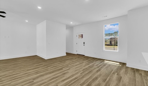 Open-concept living and dining area with white walls and light floors. Hallway leading to bedrooms.