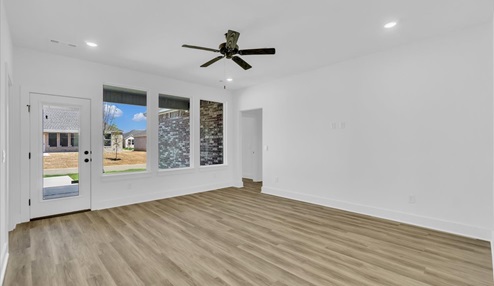 Open-concept living and dining area with white walls, light floors, three large windows and back door leading into the patio.