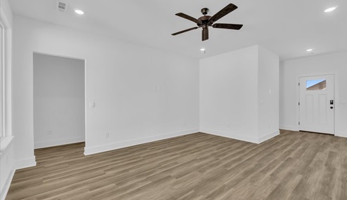 Open-concept living and dining area with white walls and light floors. Hallway leading to bedrooms.