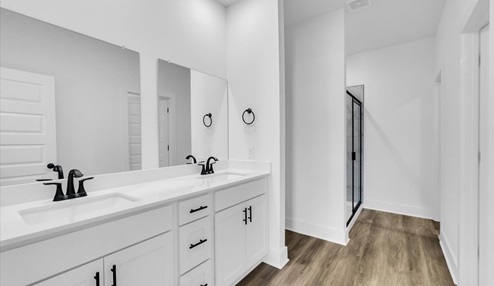 Master bathroom featuring a walk in showerwith marble tile with black trim. White vanity with double sinks. Open door leading to the masterbedroom closet.