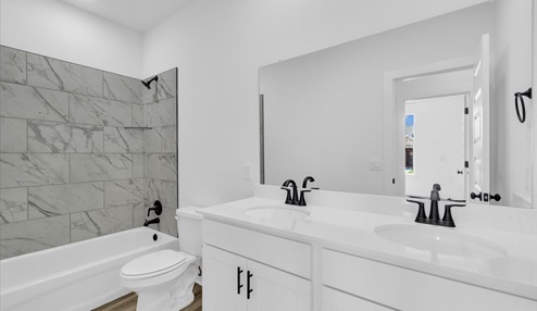 Second bath with double sinks with black ascents and white cabinets. Tub/shower combo with marble tile.