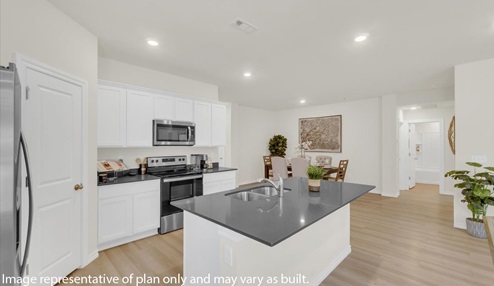 Modern open-concept living and kitchen peninsula with white cabinets and stainless steel appliances next to kitchen dinning room area.