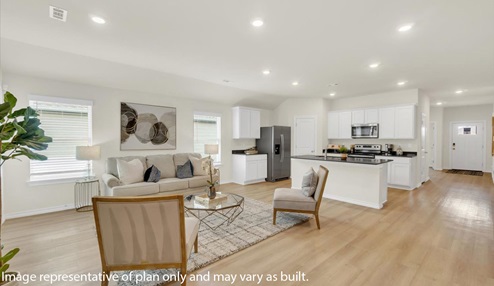 Open concept living space featuring a spacious living room area next to kitchen peninsula with white cabinets and stainless steel appliances