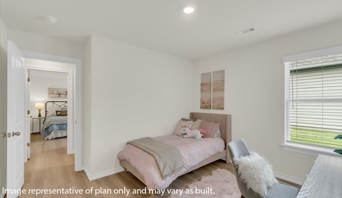 A soft, pastel-colored bedroom with a bed, pink bedding with a view into another room featuring a metal-framed bed.