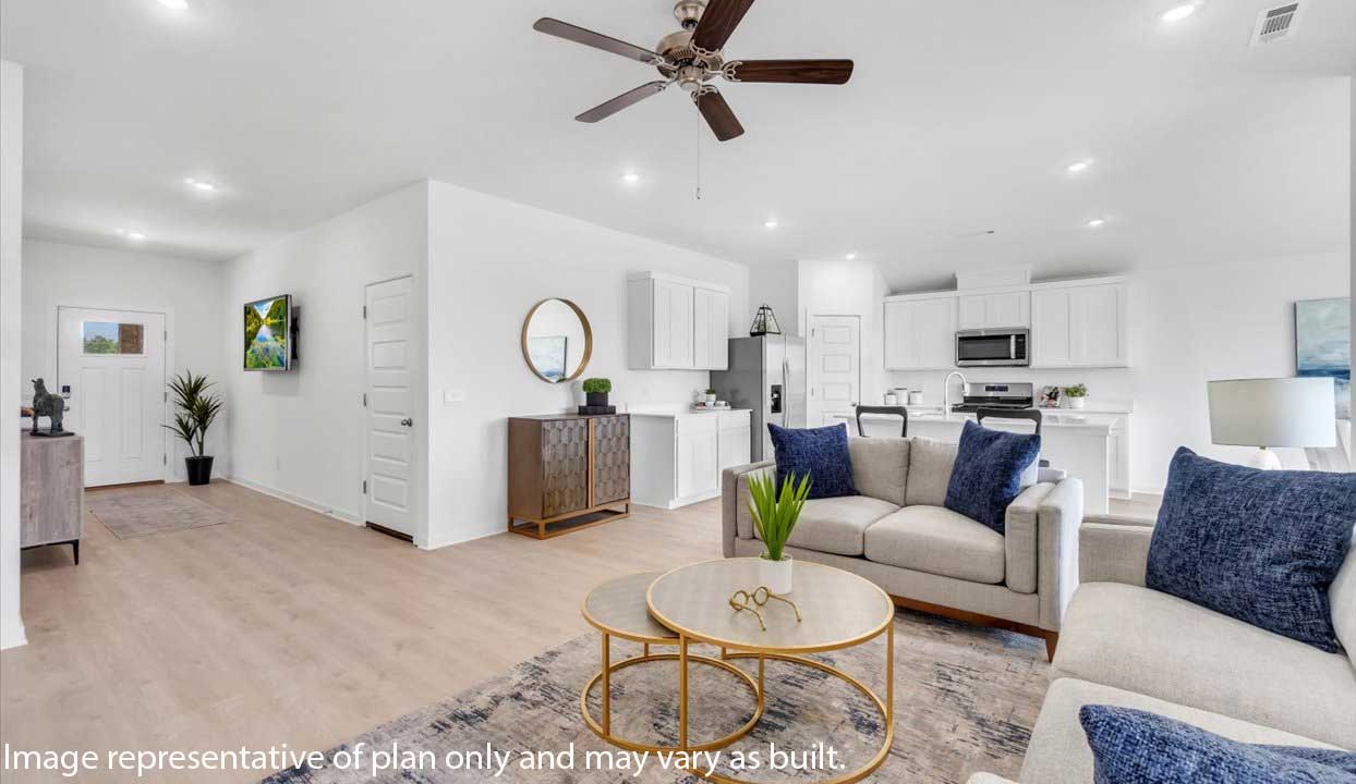 Open living area with gray sofas, blue pillows, gold coffee tables, and modern kitchen with white cabinets. Entryway includes wall TV and console.