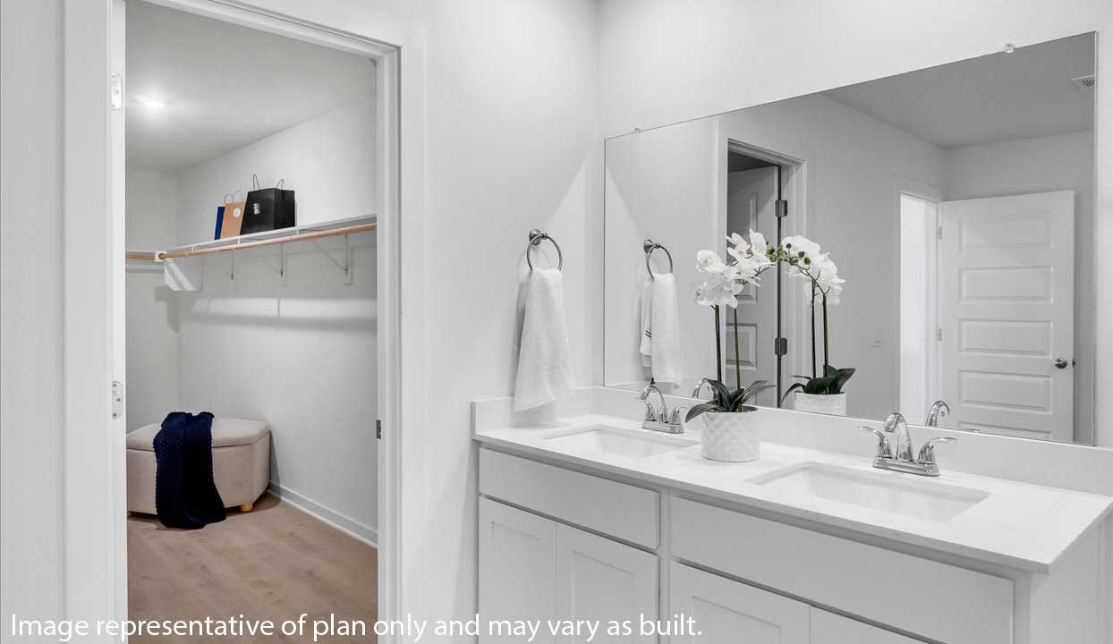 Bathroom vanity with dual sinks, large mirror, and orchid decor, adjacent to a walk-in closet with seating.