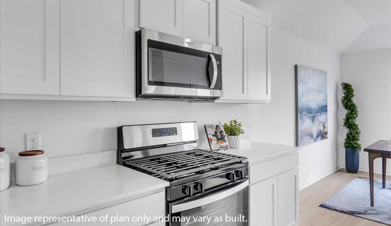 Modern kitchen detail with stainless steel stove and microwave, white cabinets, and minimal countertop decor.