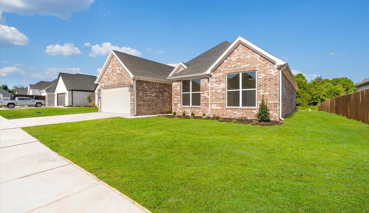 Single-story home with red brick exterior siding with a walk-up sidewalk and landscaping.