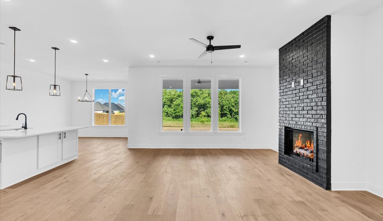 Modern open-concept living featuring brick wall and fire place, dining, and kitchen peninsula. Large windows on back wall.