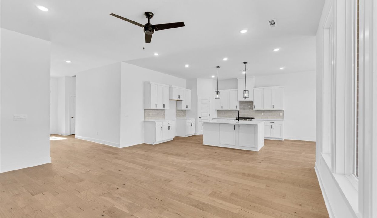 Modern open-concept living, dining, and kitchen peninsula with white cabinets and stainless steel appliances. Large windows and door leading to back porch.