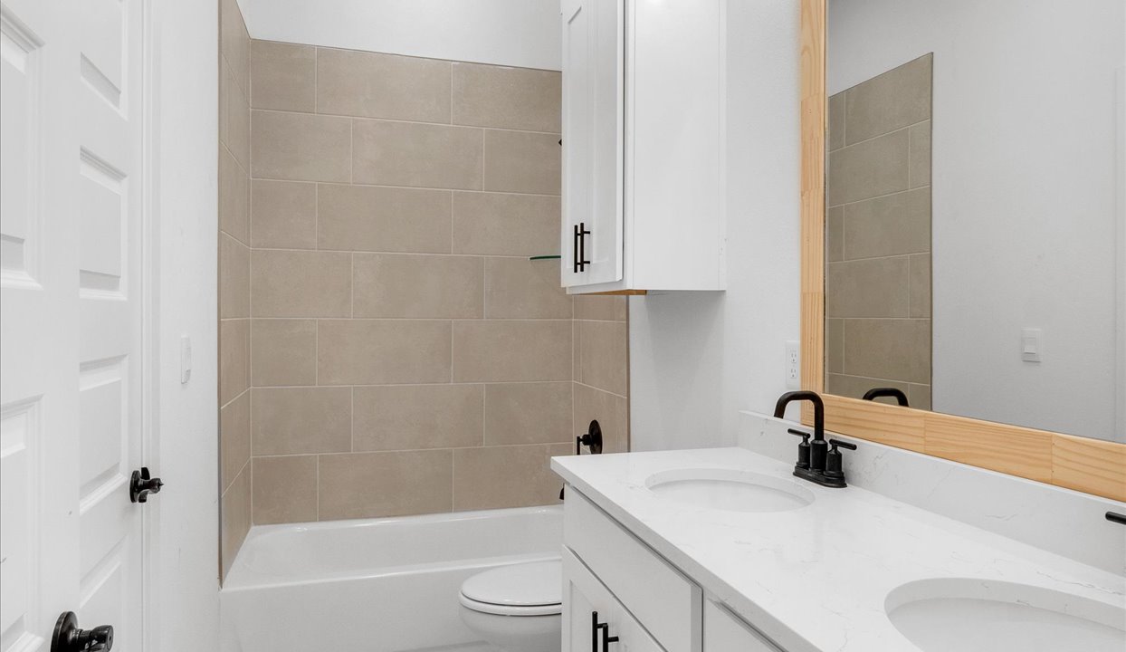 Second bath with double sinks with black ascents and white cabinets. Tub/shower combo with marble tile.