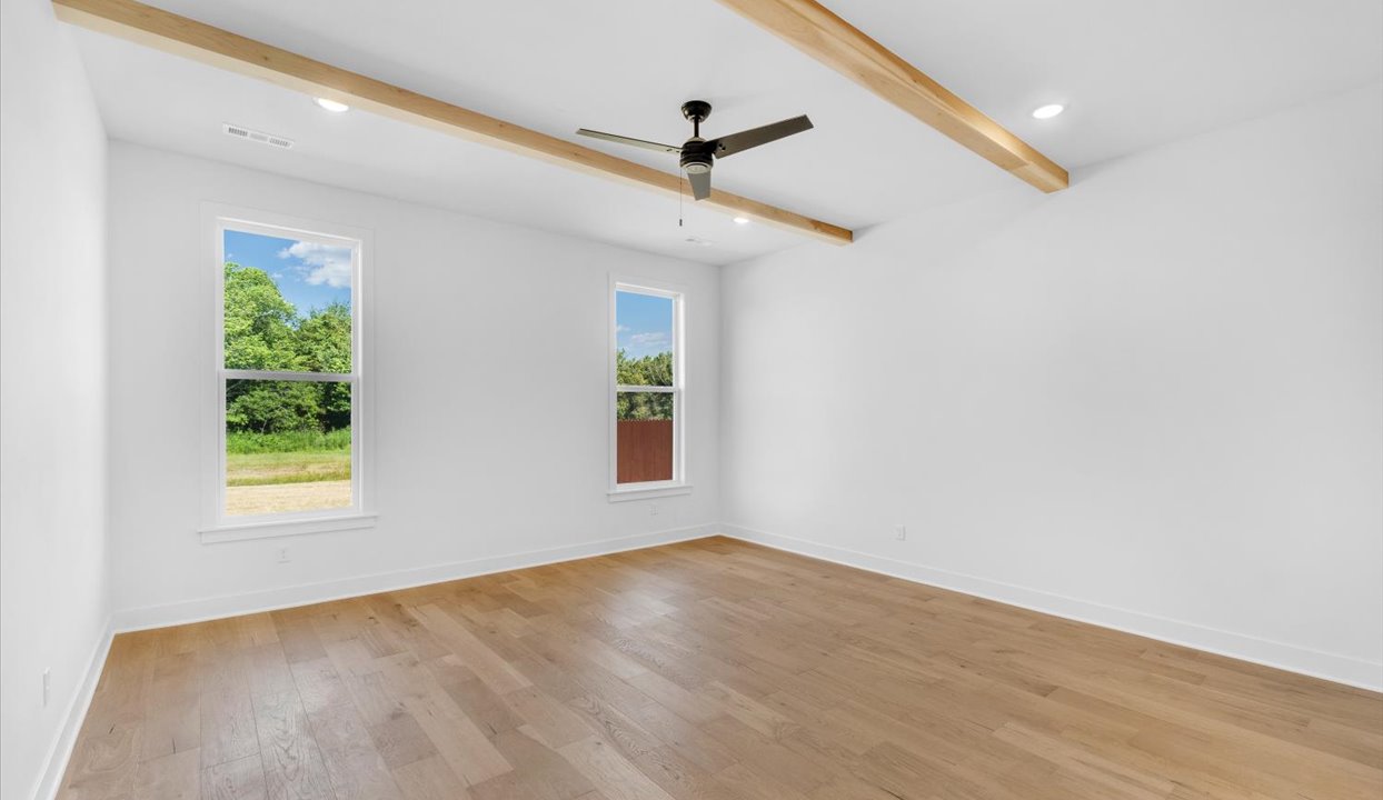Primary Bedroom with white walls, ceiling van, wood beams, and large window.