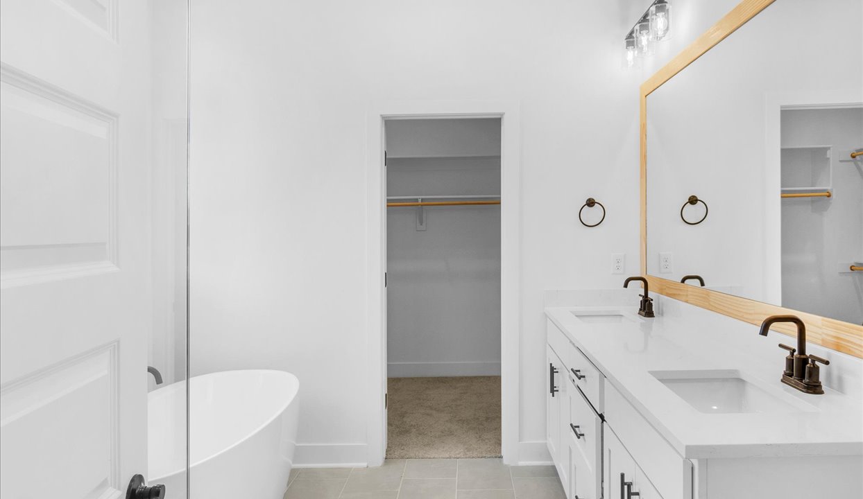 Primary bathroom featuring a walk in showerwith tile with black trim next to tub. White vanity with double sinks. Open door leading to the masterbedroom closet.