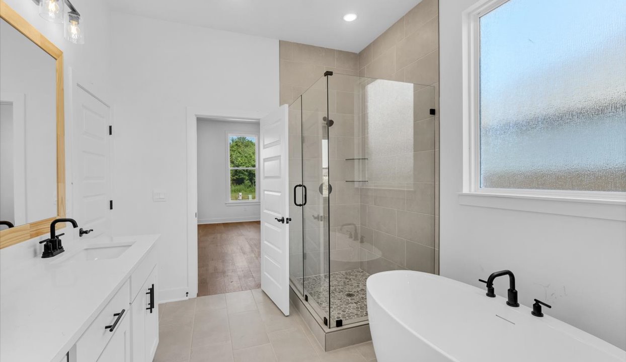 Primary bathroom featuring a walk in showerwith tile with black trim next to tub. White vanity with double sinks.