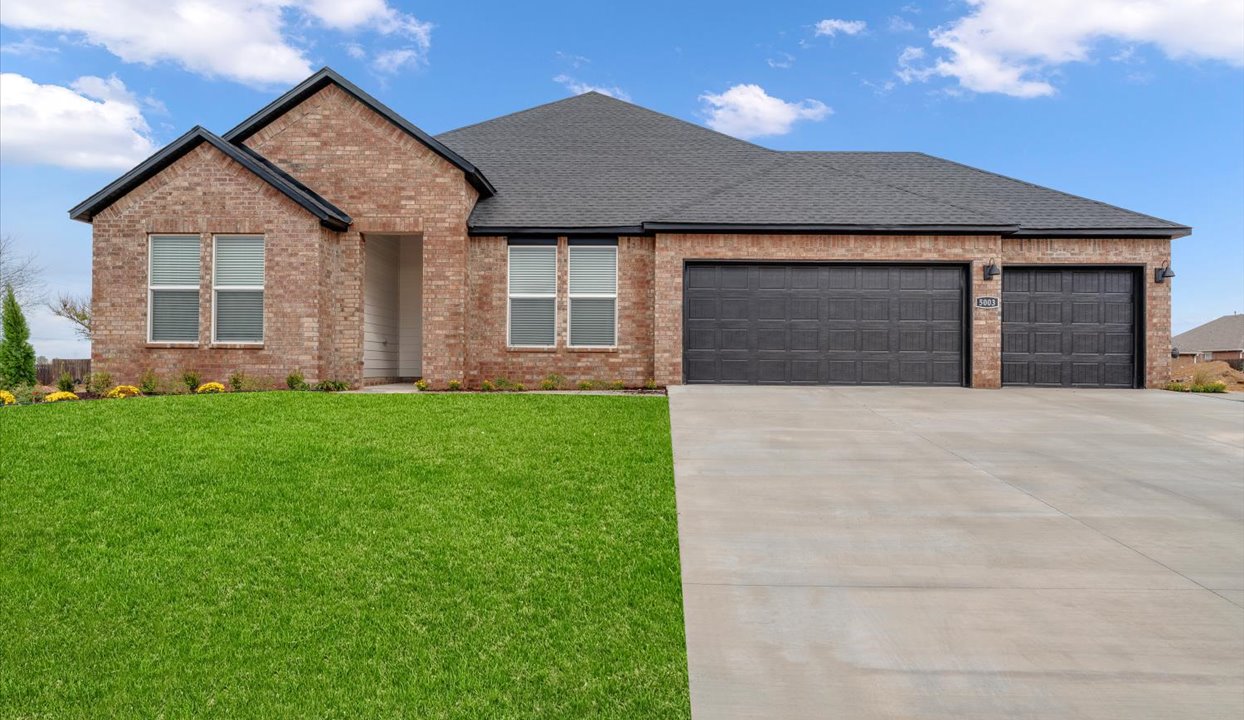 Exterior view of a modern brick house with a spacious driveway and well-maintained green lawn, featuring a dark roof and a three-car garage with matching black doors.