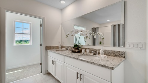 Bathroom featuring granite countertops, a sizeable wall mirror, and ample cabinetry, showing private lavatory room.