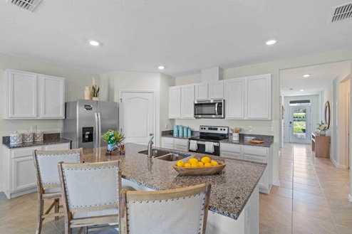Kitchen with island seating, granite counters, spacous pantry and stainless steel appliances showing entry way to home.
