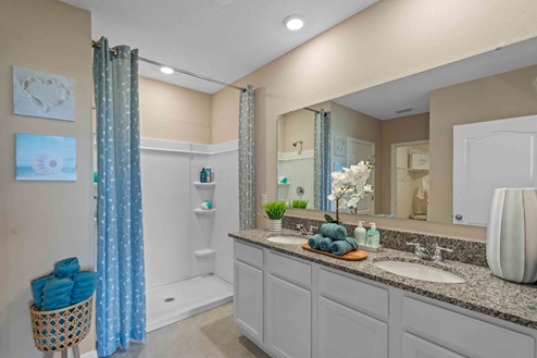 Modern bathroom with double vanity, large wall mirror, cabinets and granite countertops and walk-in shower.