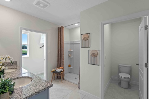Modern bathroom with double vanity, large wall mirror, cabinets and granite countertops with walk-in closet, walk-in shower, and private lavatory.