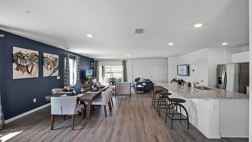 Spacious room with kitchen, living area, dining room table and wooded flooring.