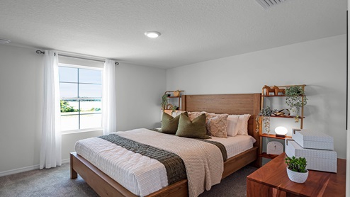 Spacious primary bedroom with king size bed, carpet flooring, natural lighting.