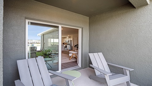 Rear of home with view of grassed backyard, porch seating and slider doors.