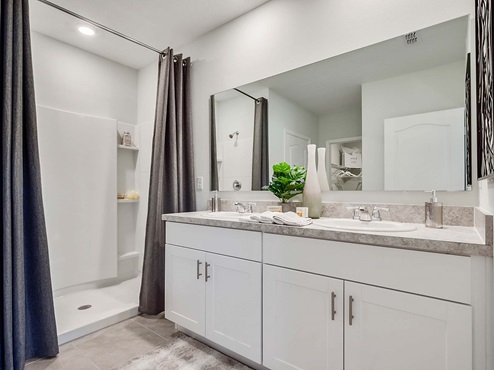 Modern bathroom with double vanity, granite countertops, large wall mirror, and cabinets alog with a walk-in shower.
