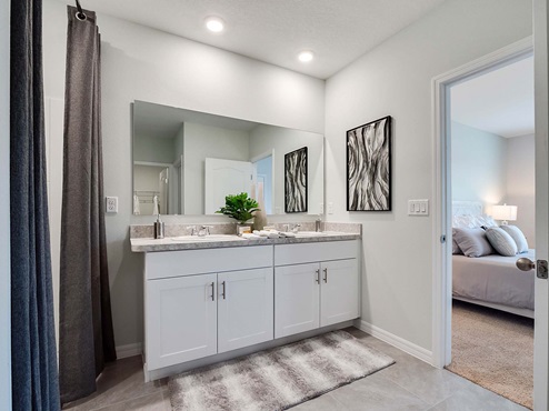 Modern bathroom with double vanity, granite countertops, large wall mirror, and cabinets alog with a walk-in shower and access to master bedroom
