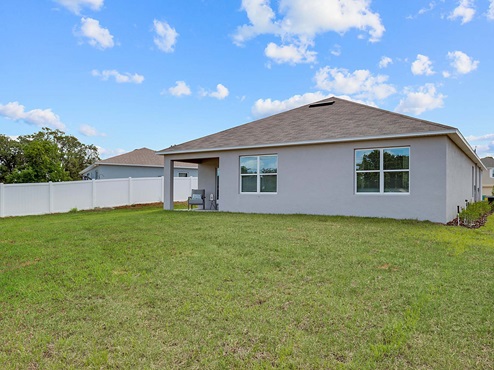 Rear of home with view of grassed backyard, porch seating.