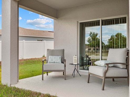 Rear of home with view of grassed backyard, porch seating and slider doors.