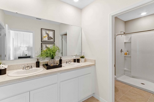 Bathroom featuring granite countertops, a sizeable wall mirror, and ample cabinetry, along with a walk-in shower.