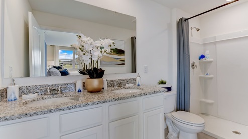 Modern bathroom with double vanity, large wall mirror, cabinets and granite countertops along with toilet and walk-in shower.