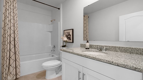 Modern bathroom with single vanity, large wall mirror, cabinets and granite countertops along with shower and toilet