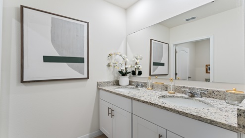 Modern bathroom with double vanity, granite countertops, cabinets, large mirror.