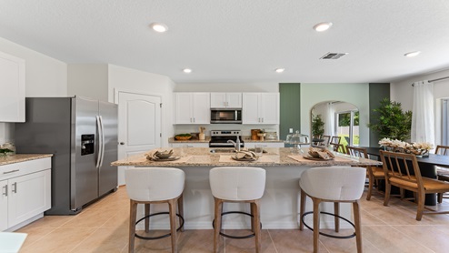 Kitchen with island seating, granite counters, spacous pantry and stainless steel appliances overseeing dining room.