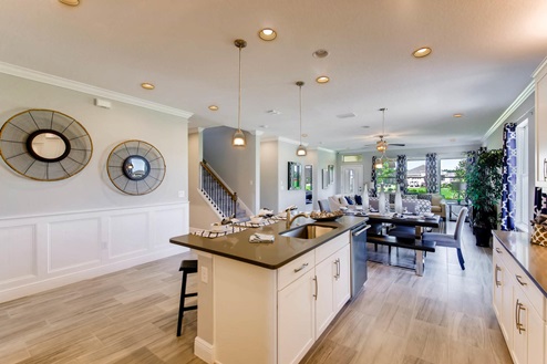 Kitchen with island seating, granite counters, and stainless steel appliances with access to staircase overseeing living area.