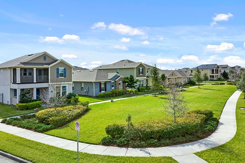 Side walk with bright green grass by two-story houses.