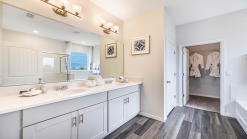 Modern bathroom with double vanity, large wall mirror, cabinets and quartz countertops showing access to master bedroom.