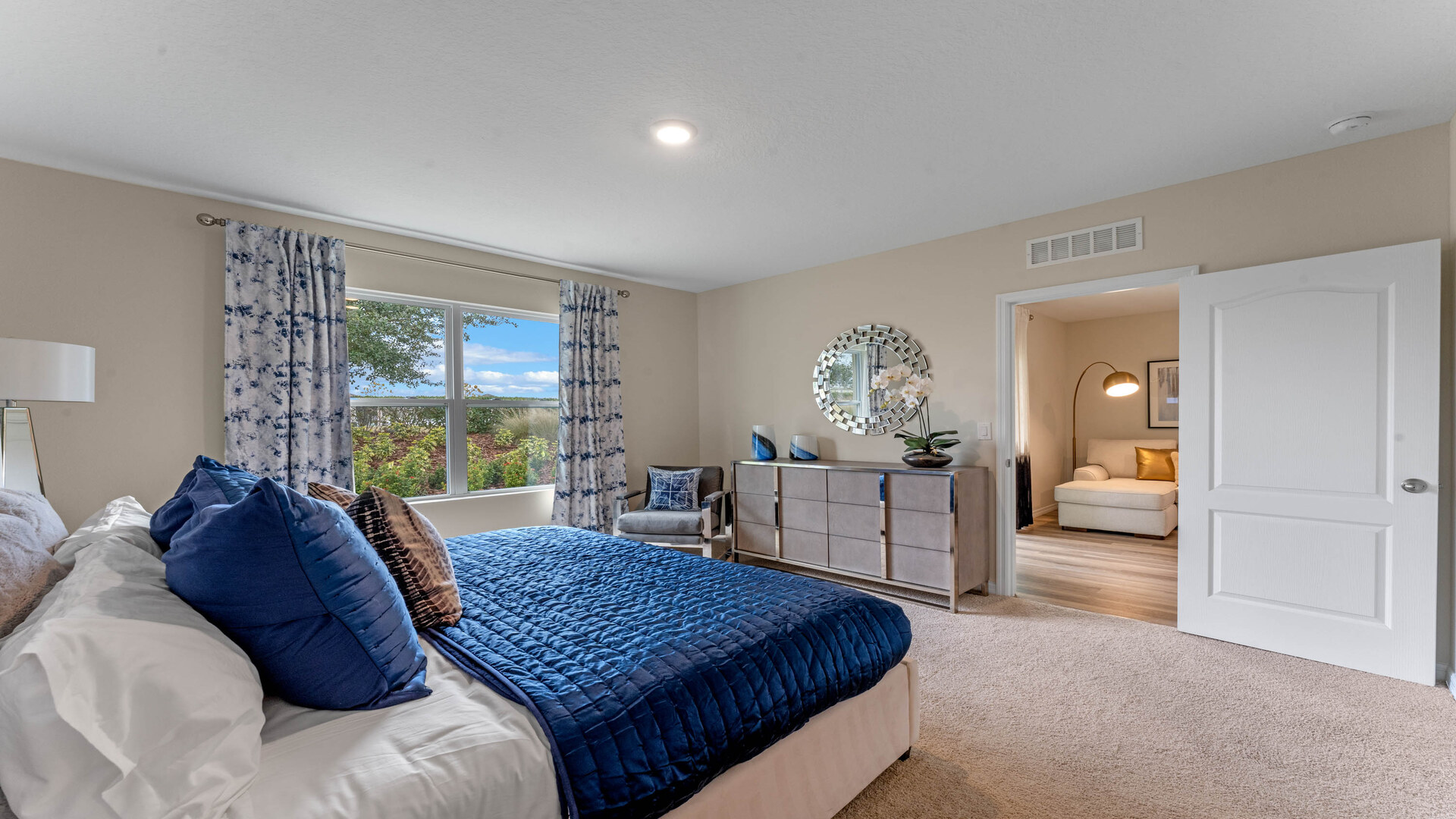 Spacious primary bedroom with king size bed, carpet flooring, natural lighting.