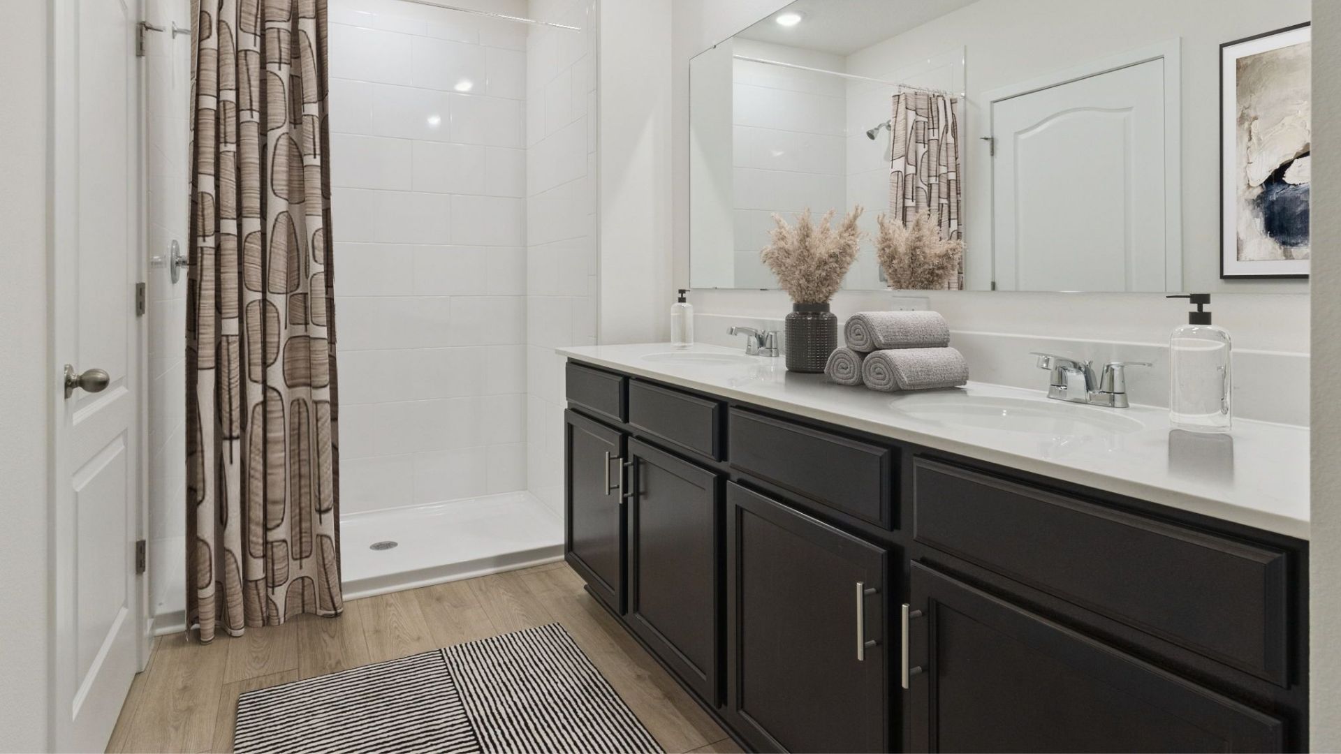 Modern bathroom with double vanity, large wall mirror, cabinets and quartz countertops along with toilet and walk-in shower