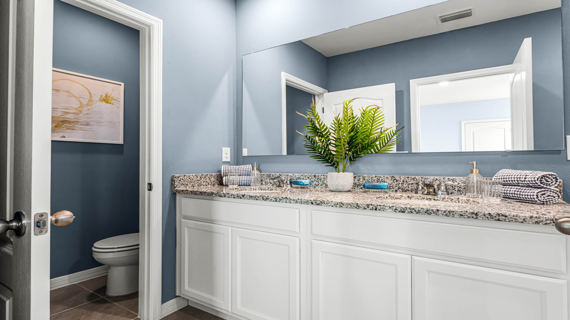 Modern bathroom with single vanity, large wall mirror, cabinets and granite countertops along with toilet and shower